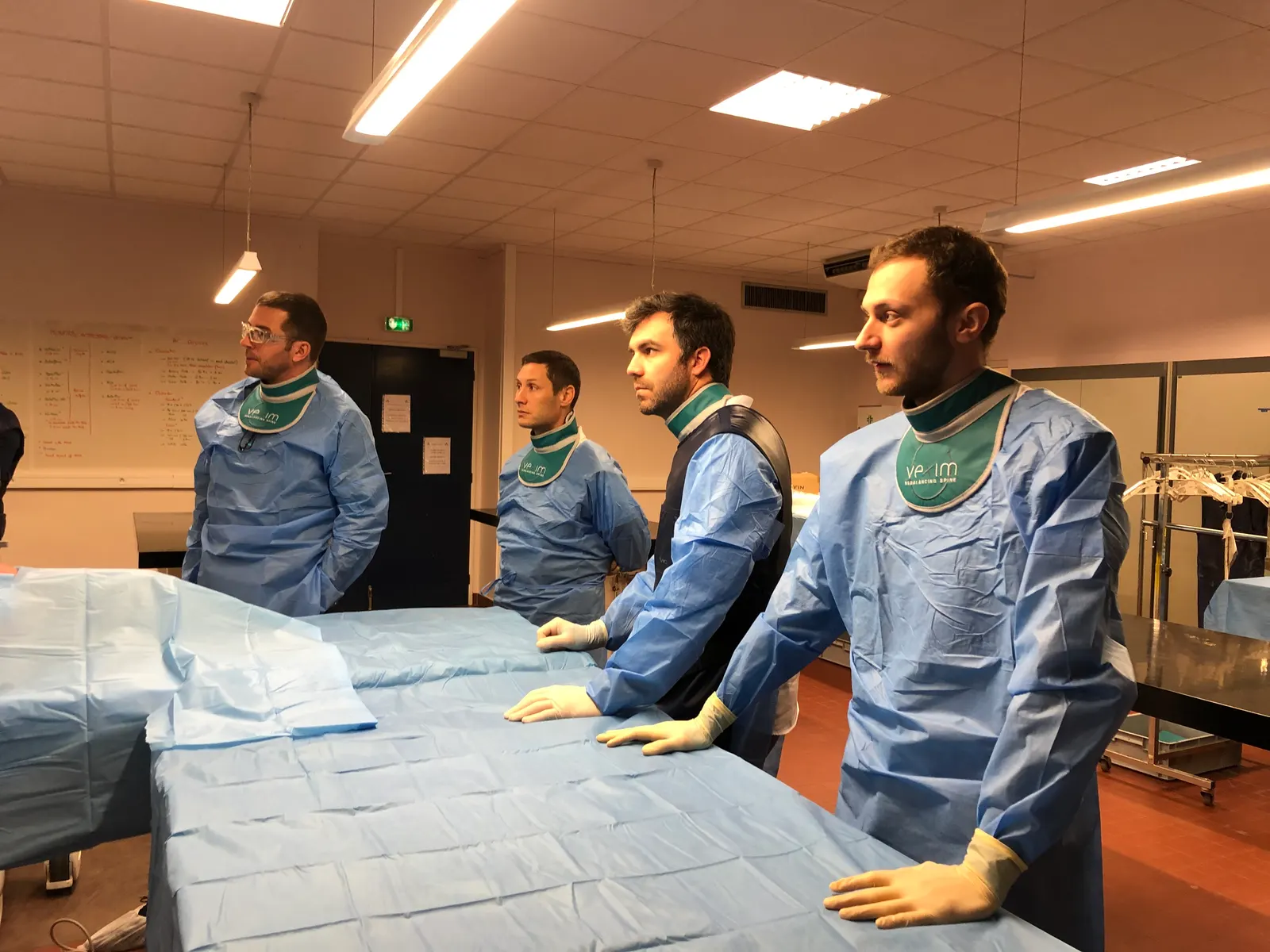 Quatre personnes en blouse chirurgicale et gants, debout autour d'une table couverte de champs opératoires, dans un laboratoire d'anatomie